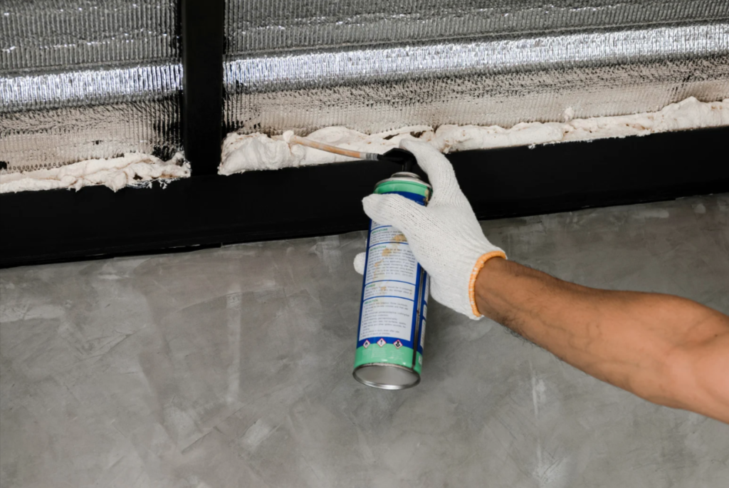 Worker applying expanding foam insulation to seal a roof gap during an emergency roof leak repair